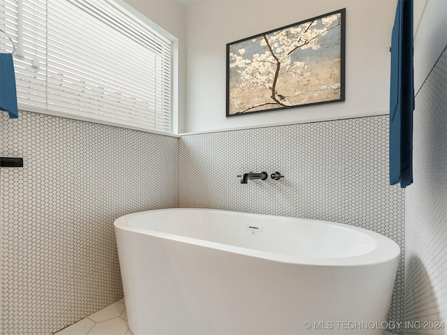 bathroom with tile patterned floors, a tub to relax in, sink, and tile walls