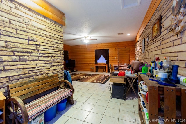 interior space featuring ceiling fan, wood walls, light tile patterned floors, and a textured ceiling