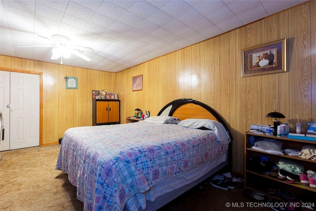 carpeted bedroom with ceiling fan, a closet, and wood walls