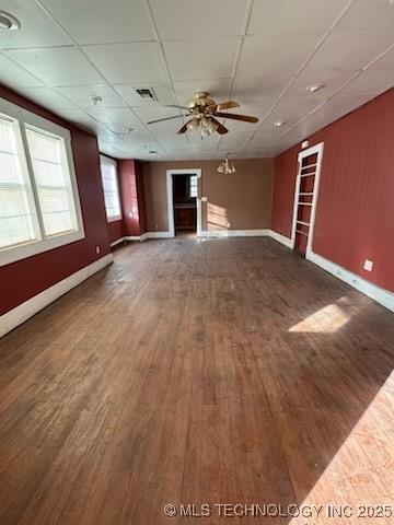 unfurnished living room featuring dark wood-type flooring, a drop ceiling, and ceiling fan