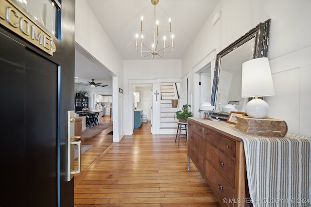 entrance foyer featuring light hardwood / wood-style flooring, a towering ceiling, and ceiling fan with notable chandelier