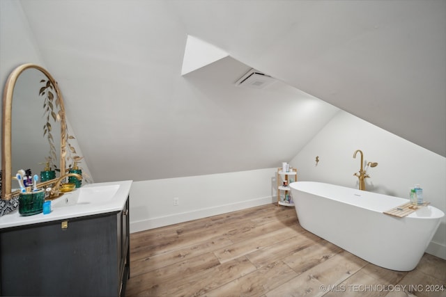 bathroom with lofted ceiling, wood-type flooring, a tub to relax in, and vanity