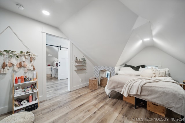 bedroom with a barn door, light wood-type flooring, and lofted ceiling