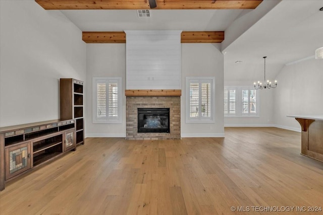 unfurnished living room with light wood-type flooring, an inviting chandelier, a brick fireplace, and plenty of natural light