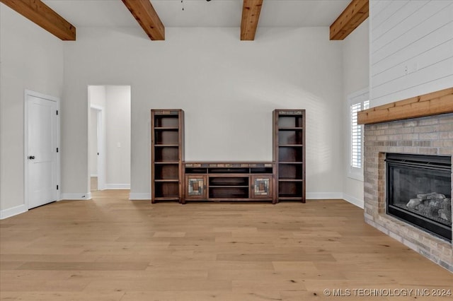 unfurnished living room featuring a fireplace, a towering ceiling, light wood-type flooring, and beamed ceiling