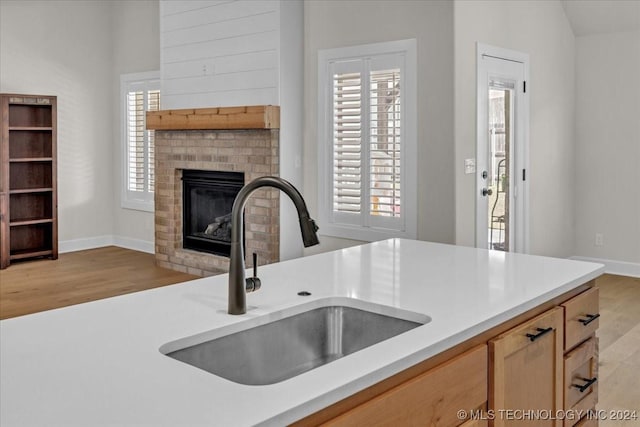 kitchen with light brown cabinetry, vaulted ceiling, sink, a fireplace, and light hardwood / wood-style floors