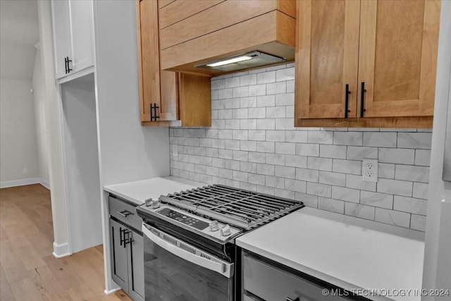 kitchen featuring white cabinets, decorative backsplash, light wood-type flooring, stainless steel range, and custom range hood