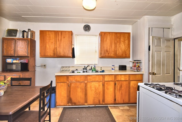 kitchen with white gas range, sink, and light tile patterned floors