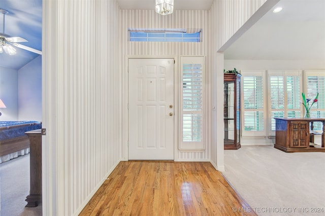 foyer entrance with ceiling fan with notable chandelier, lofted ceiling, and light wood-type flooring