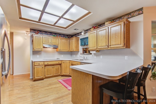 kitchen featuring a kitchen breakfast bar, light hardwood / wood-style flooring, stainless steel fridge, stovetop, and kitchen peninsula