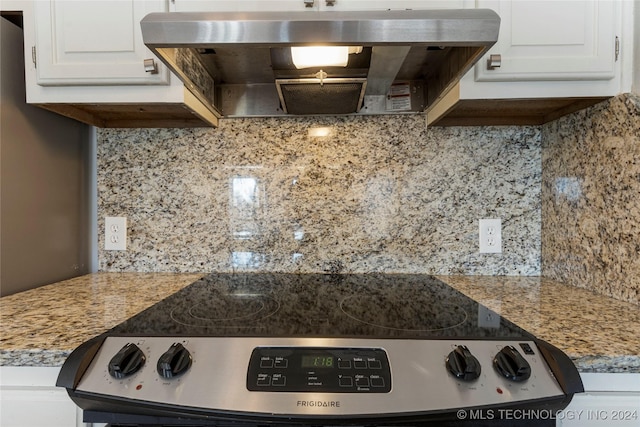 kitchen with backsplash, white cabinets, stainless steel stove, and range hood