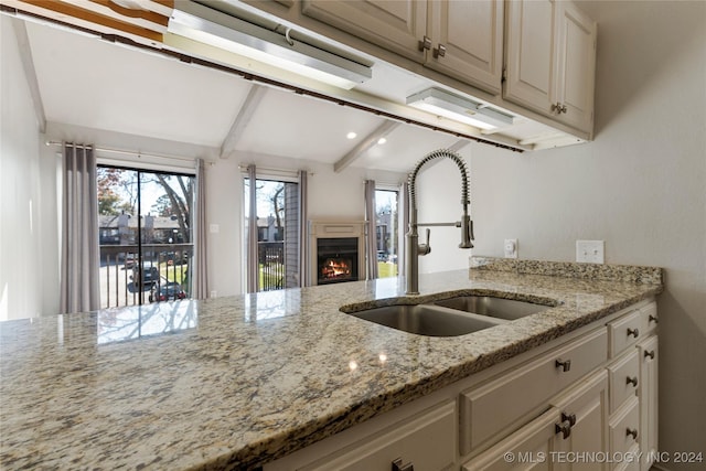 kitchen with beamed ceiling, light stone countertops, sink, and cream cabinetry