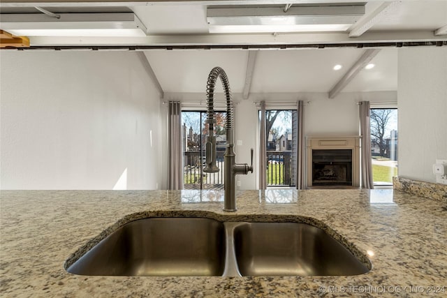 kitchen with beamed ceiling, light stone counters, and sink