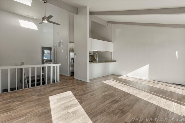 unfurnished living room featuring a skylight, ceiling fan, wood-type flooring, beam ceiling, and high vaulted ceiling