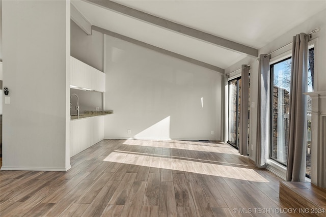 unfurnished living room with beamed ceiling, light wood-type flooring, and high vaulted ceiling