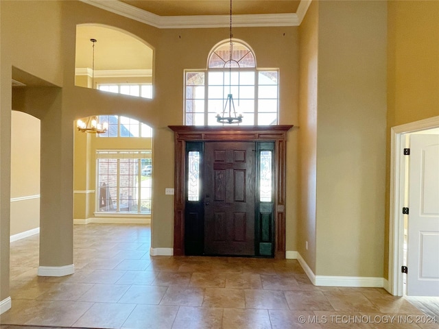 tiled entrance foyer with crown molding, a towering ceiling, and a chandelier