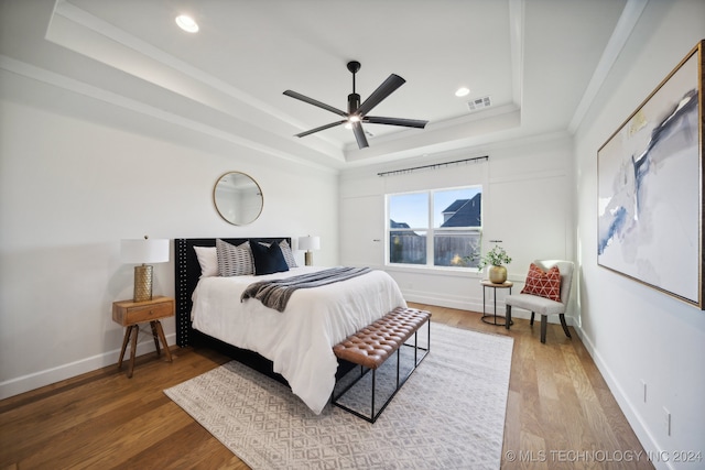 bedroom featuring hardwood / wood-style floors, ceiling fan, ornamental molding, and a tray ceiling