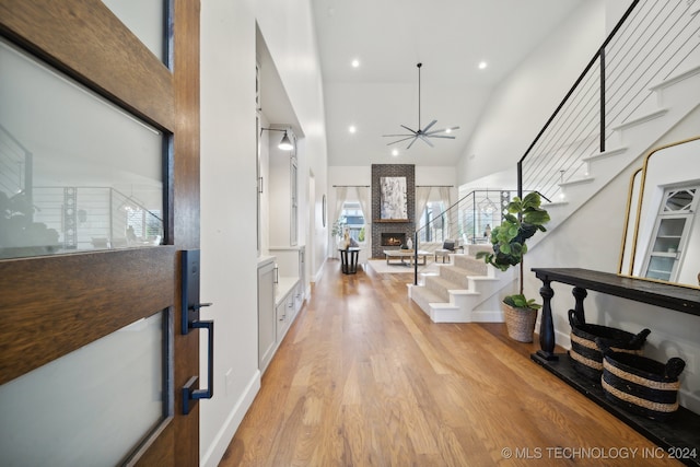 foyer with ceiling fan, light wood-type flooring, high vaulted ceiling, and a brick fireplace