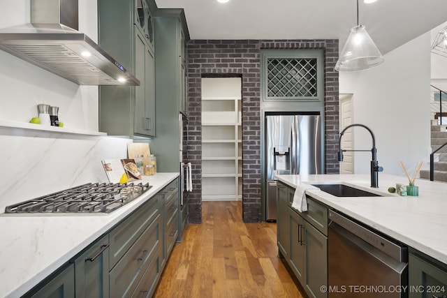 kitchen featuring appliances with stainless steel finishes, sink, wall chimney range hood, light hardwood / wood-style flooring, and hanging light fixtures