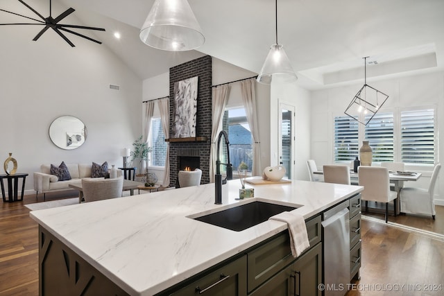 kitchen featuring sink, hanging light fixtures, dark wood-type flooring, an island with sink, and a fireplace