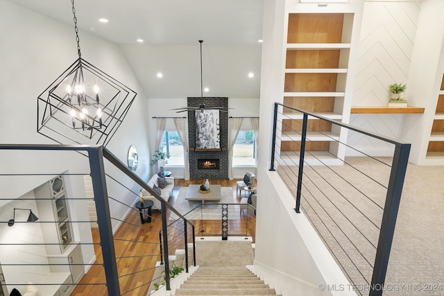 stairway with a chandelier, vaulted ceiling, and a brick fireplace