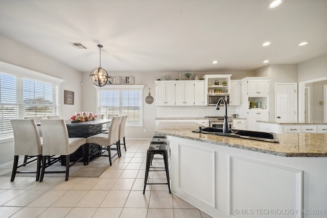 kitchen with pendant lighting, an inviting chandelier, an island with sink, light stone counters, and white cabinetry