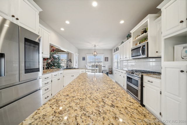 kitchen featuring decorative backsplash, light stone countertops, stainless steel appliances, decorative light fixtures, and white cabinetry