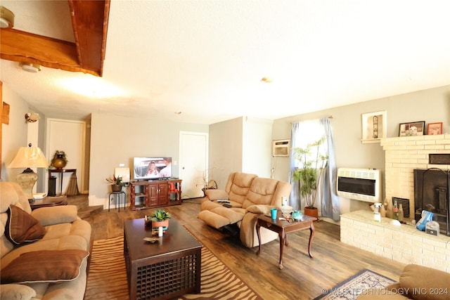 living room featuring wood-type flooring, heating unit, a brick fireplace, and an AC wall unit