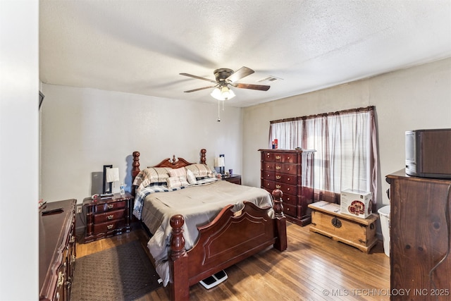 bedroom with ceiling fan, hardwood / wood-style floors, and a textured ceiling