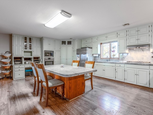 kitchen with white cabinetry, a center island, stainless steel appliances, light hardwood / wood-style flooring, and a breakfast bar area