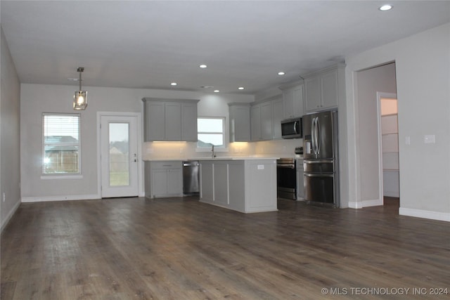 kitchen with appliances with stainless steel finishes, decorative light fixtures, a kitchen island, and dark wood-type flooring