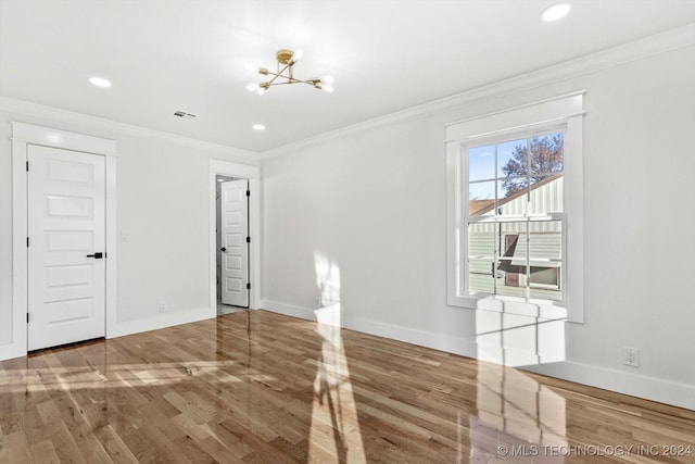 empty room featuring a chandelier, hardwood / wood-style floors, and crown molding