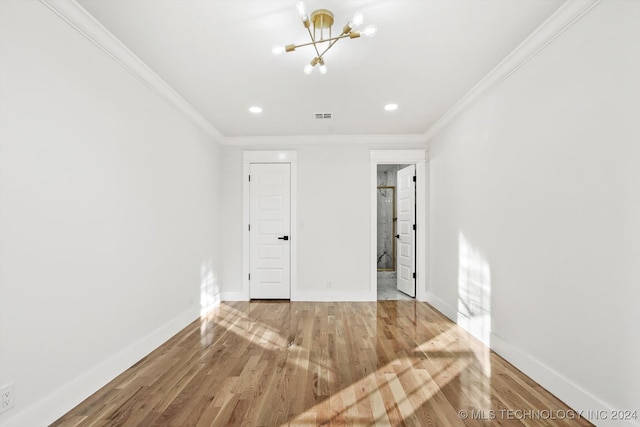 unfurnished bedroom featuring hardwood / wood-style flooring, crown molding, and a notable chandelier