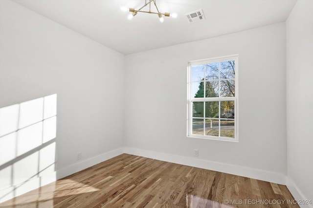 unfurnished room featuring an inviting chandelier and hardwood / wood-style flooring