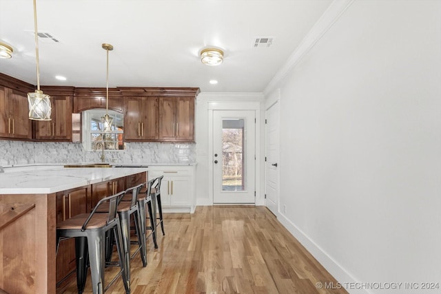 kitchen with tasteful backsplash, light stone counters, light hardwood / wood-style flooring, decorative light fixtures, and a breakfast bar