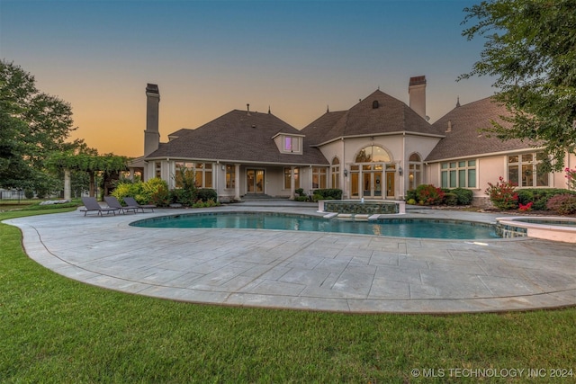 pool at dusk with an in ground hot tub, a yard, pool water feature, and a patio area