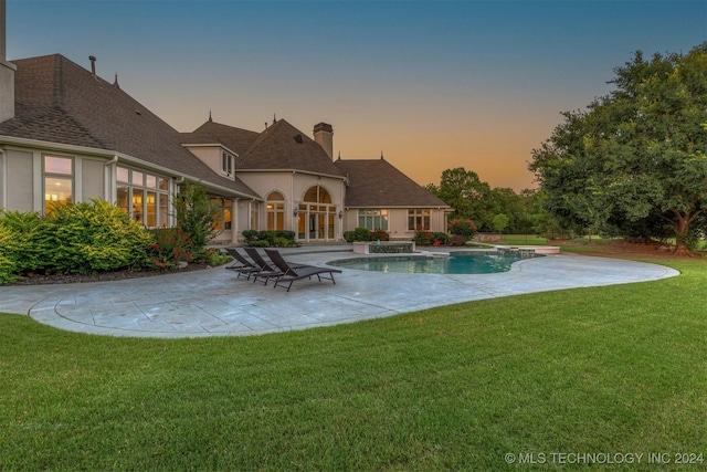 pool at dusk featuring a patio area, a jacuzzi, and a yard