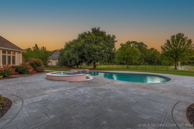 pool at dusk with an in ground hot tub, a patio area, and a lawn