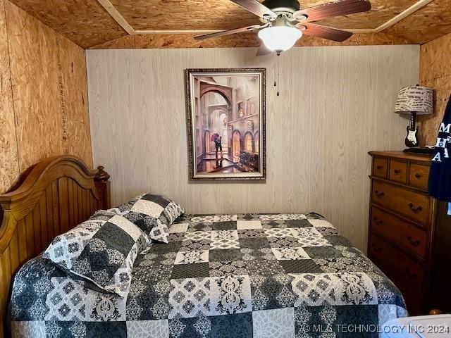 bedroom featuring ceiling fan and wooden walls