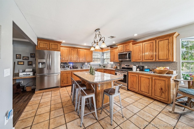 kitchen with a wealth of natural light, a kitchen island, stainless steel appliances, and decorative light fixtures