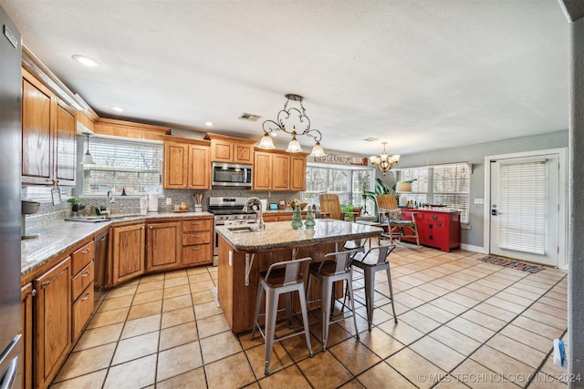 kitchen with a chandelier, stainless steel appliances, a wealth of natural light, and an island with sink