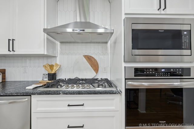 kitchen featuring backsplash, dark stone counters, wall chimney exhaust hood, appliances with stainless steel finishes, and white cabinetry