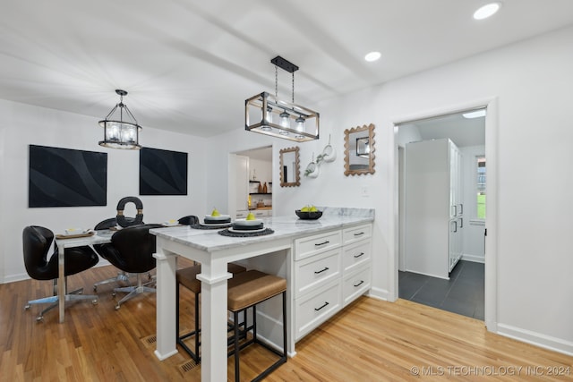 kitchen featuring white cabinetry, light stone countertops, decorative light fixtures, a breakfast bar, and light wood-type flooring