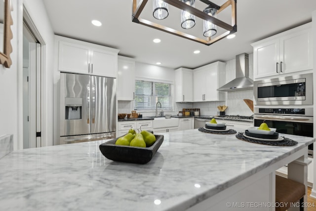 kitchen featuring wall chimney range hood, dark stone countertops, appliances with stainless steel finishes, tasteful backsplash, and white cabinetry