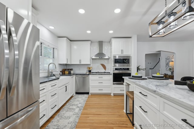 kitchen featuring stainless steel appliances, white cabinetry, and wall chimney range hood