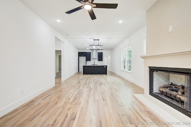 unfurnished living room with ceiling fan with notable chandelier, wood-type flooring, and sink