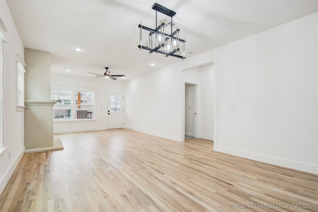 unfurnished living room featuring ceiling fan with notable chandelier and light wood-type flooring