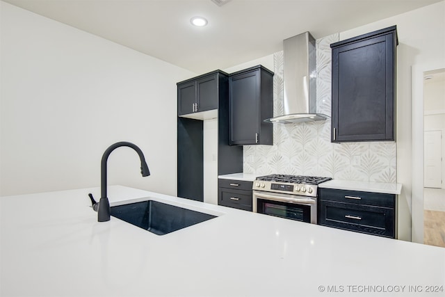 kitchen featuring hardwood / wood-style floors, high end range, wall chimney range hood, sink, and tasteful backsplash