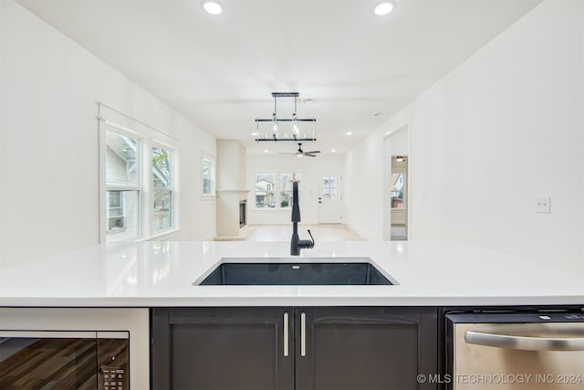 kitchen with sink, beverage cooler, stainless steel dishwasher, decorative light fixtures, and ceiling fan with notable chandelier