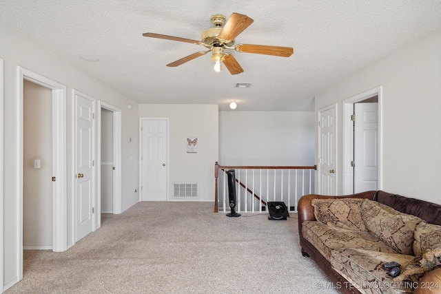 living area with ceiling fan, light colored carpet, and a textured ceiling